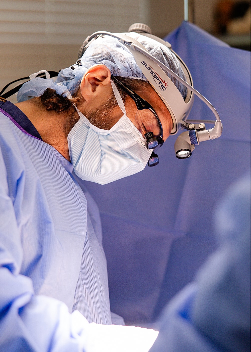 Surgeon focused on operation, wearing surgical gear.