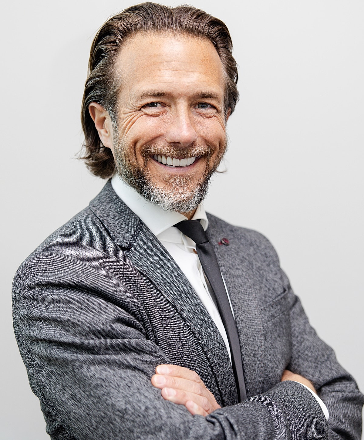 Smiling man in a gray suit with crossed arms.