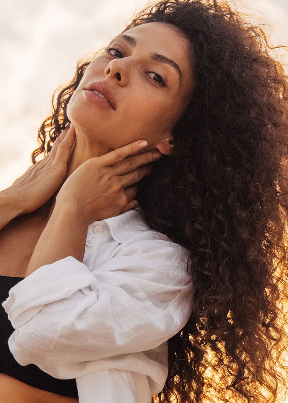 Woman with curly hair and white shirt outdoors.