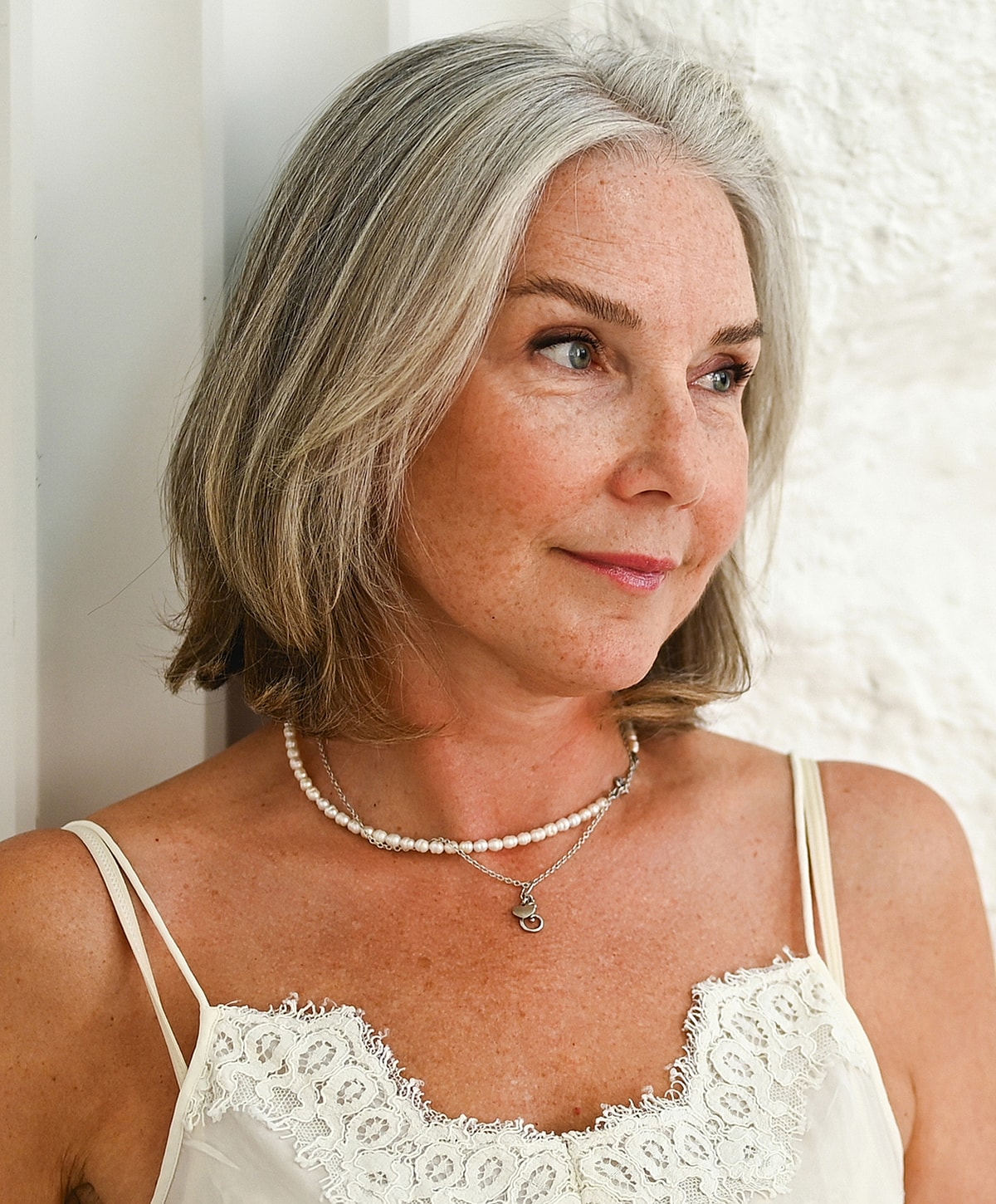 Older woman with gray hair and layered necklaces.