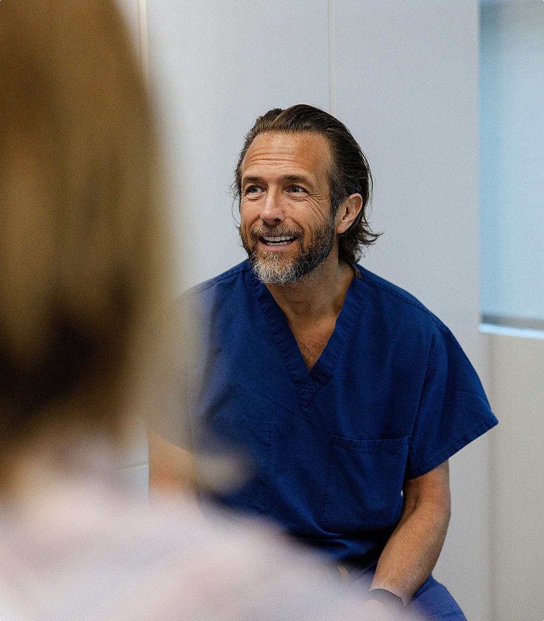Smiling man in blue scrubs during consultation.